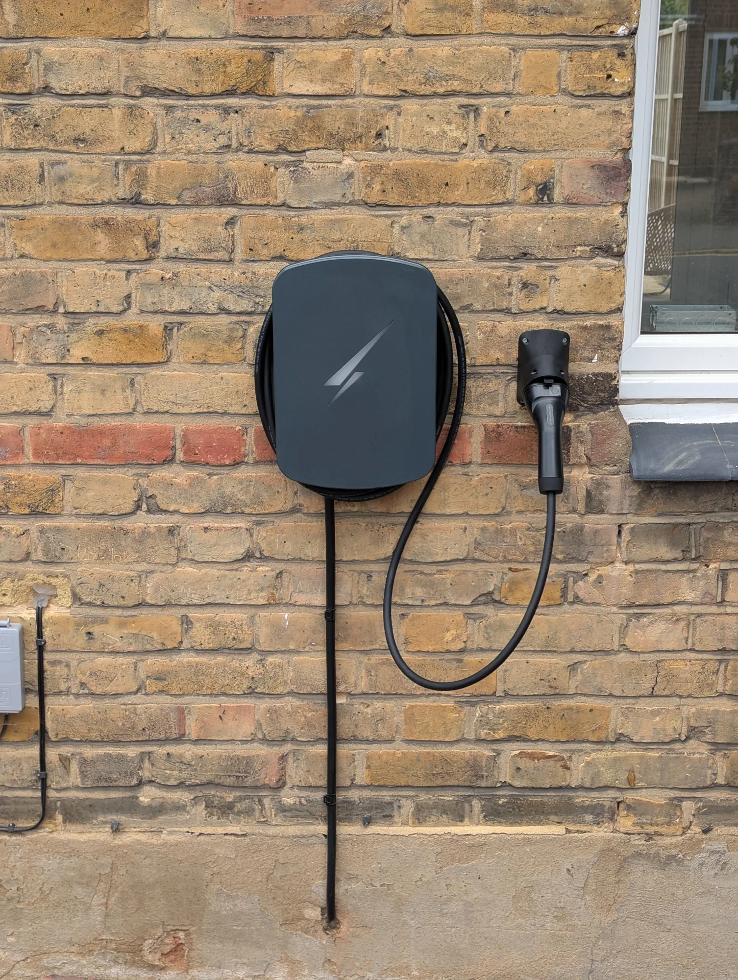 Wall-mounted tethered EV charger with coiled cable and docked connector
